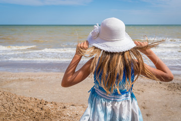 Beautiful girl in white hat on the seashore over blue sky background