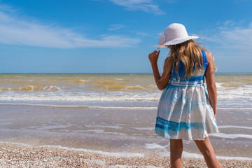 Girl in white hat and colorful dress on the seashore over blue sky background