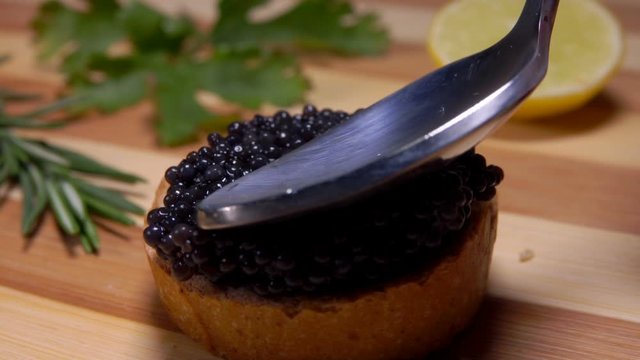 Spoon presses the hill of black caviar on a piece of white bread