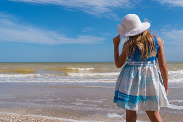 Girl in white hat and beautiful dress on the seashore over blue sky background