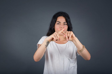 Young beautiful brunette girl wearing casual clothes over isolated background standing against gray wall. Has rejection angry expression crossing fingers doing negative sign.