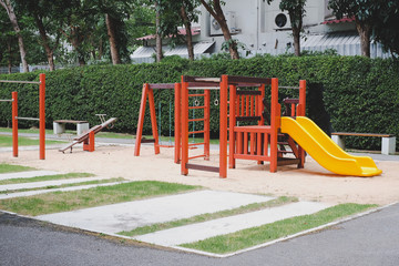 Children playground on yard activities in public park surrounded by green trees. Children run, slide, swing,seesaw on modern playground. Urban neighborhood childhood concept