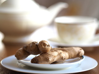teapot with a cup of ginger tea and a natural ginger root on a plate