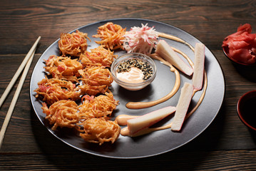 Close up view of delicious sushi with crab sticks on black plate served on the wooden table, decorated with chopsticks, bowl of soy sauce, and ginger