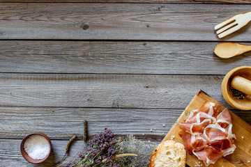 Prosciutto ham and bread on a wooden background. Italian cuisine. Rustic style.