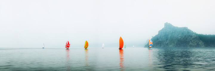 Fototapeta premium Yacht regatta with an orange sail in a foggy morning floats on the sea