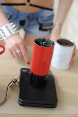 Barista girl turns on electronic scales with red manual coffee grinder. Brewinf process