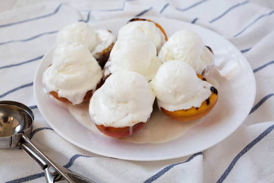 Homemade grilled peaches with vanilla ice cream on a white plate, side view. Close-up.