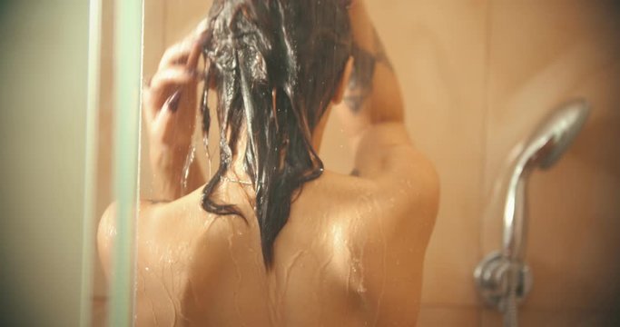 A woman with tattoos standing in her bathroom and taking a shower - washing her hair