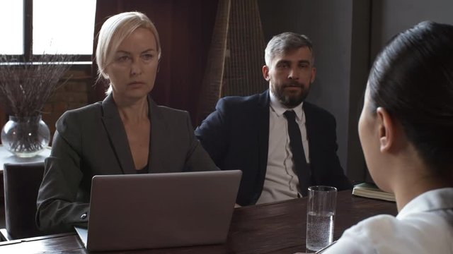 Over-shoulder shot of middle-aged Caucasian male and female corporate executives in formal attire sitting at private meeting room in restaurant and interviewing Asian woman, making notes on laptop