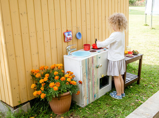 Young girl child playing outdoors in so called mud kitchen, where you can make fake food, play with sand, dirt, water, plants and make a mess, it develops imagination and exploration.