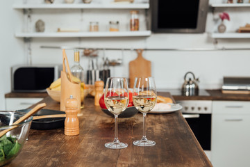 wine glasses with wine, food and cooking utensils on table in kitchen
