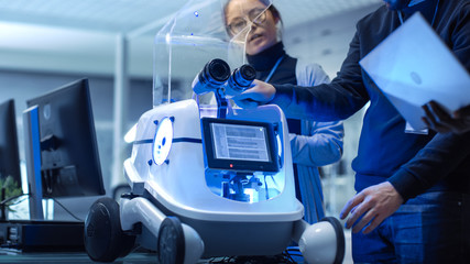 Close-up Shot of a Robot in a Modern Laboratory/ Research Center. Multi Ethnic Team of Male and Female Leading Scientists are Working with Robot.
