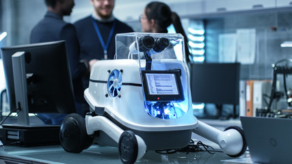 Shot of a Working Robot Prototype in a Modern Laboratory/ Research Center Creating Robotics. Multiethnic Group of Young Scientists have Discussion on backgrounds.