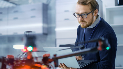 Male Engineer Programs Drone while Holding Laptop in His Hands. He Works in a Bright Modern...