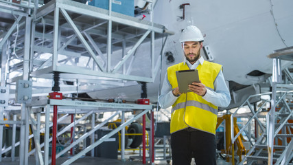 Aircraft Maintenance Mechanics Moving through Hangar. Holding Tablet Computer