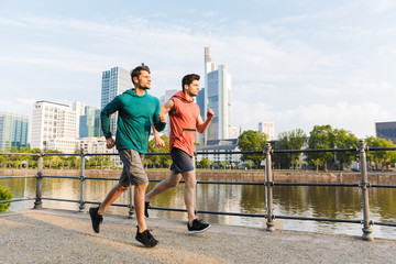 Photo of two strong sporty men doing workout and running on city riverfront