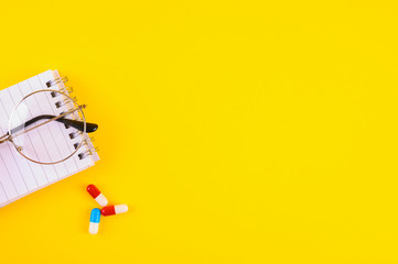 Medikamente mit einem Notizblock und einer Brille auf gelben Hintergrund