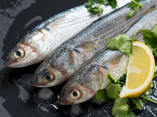 Fresh mullet on a stone black background with spices and lemon, seasoned with salt and pink pepper. View from above. Top View. Sea fish. Close-up