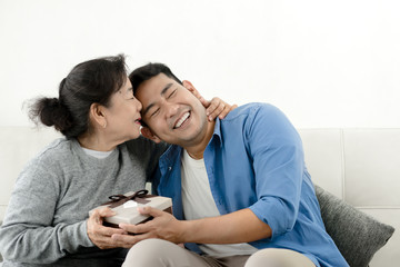 Happy Asian man giving gift box to his mother for Mother's Day celebration.