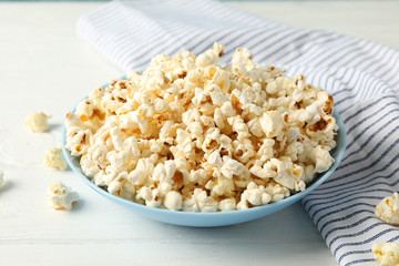 Towel and plate with popcorn on white wood background, copy space
