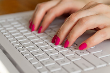 Hands of a girl typing on a white laptop keyboard. Closeup