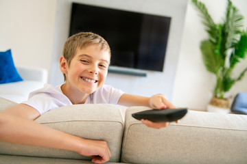 A boy holding remote control and watching TV show