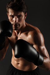 Fototapeta na wymiar Handsome young strong sportsman boxer in gloves make exercises boxing isolated over black wall background.