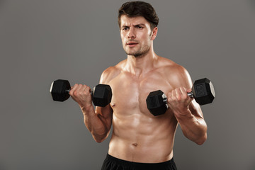 Fototapeta na wymiar Handsome young strong sportsman posing isolated over grey wall background make exercises with dumbbells for arms.