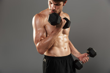 Handsome young strong sportsman posing isolated over grey wall background make exercises with...
