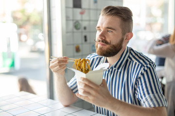 Positive young stylish guy eating chinese noodles in a cafe during a break at work. The concept of rest and healthy snack.