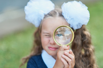 Portrait of a beautiful young Schoolgirl looking through a magnifying glass and sitting at a desk