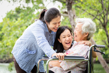 Asian family,senior grandmother,mother,smiling daughter enjoy,hugging in park,patient elderly laugh talk funny with family in wheelchair,happy woman,child girl care with her,love,relationship concept