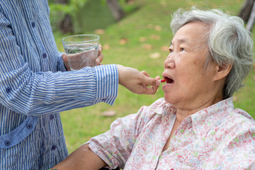 Naklejka premium Asian daughter or caregiver medicine pills or capsules in hand or finger and water,giving pills to senior mother,sick elderly woman eating vitamin,antibiotic,painkiller in outdoor park,health care 