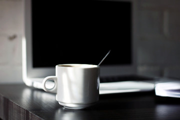 Coffee mug on a desk, with a laptop and a notebook.