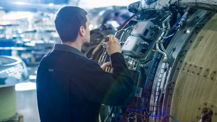 Aircraft Maintenance Mechanic Inspecting with Flashlight Airplane Jet Engine in Hangar
