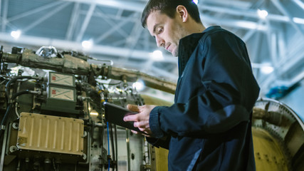 Aircraft Maintenance Mechanic Inspecting and Working on Airplane Jet Engine in Hangar