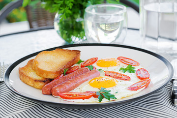 English breakfast on summer terrace: fried eggs, sausage, tomatoes, and toasts. Cup of coffee. Close up of hotel breakfast.