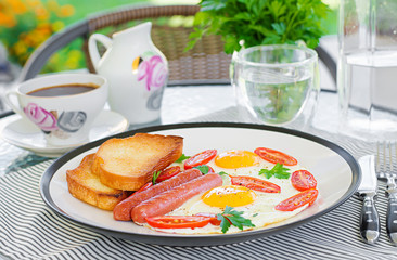 English breakfast on summer terrace: fried eggs, sausage, tomatoes, and toasts. Cup of coffee. Close up of hotel breakfast.