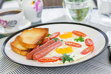English breakfast on summer terrace: fried eggs, sausage, tomatoes, and toasts. Cup of coffee. Close up of hotel breakfast.