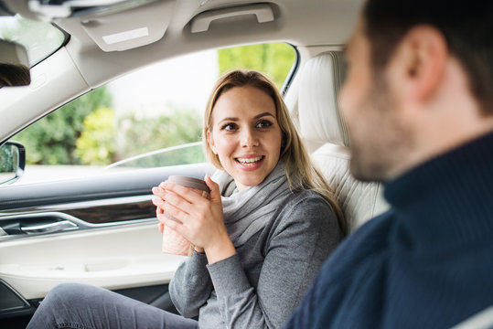 Happy Young Couple With Coffee Sitting In Car, Talking.