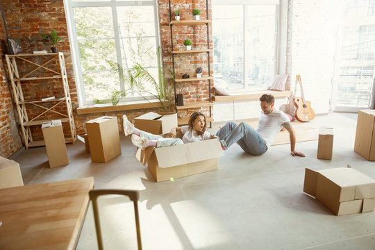 Young couple moved to a new house or apartment. Having fun with cardboard boxes, relaxing after cleaning and unpacking at moved day. Look happy. Family, moving, relations, first home concept.