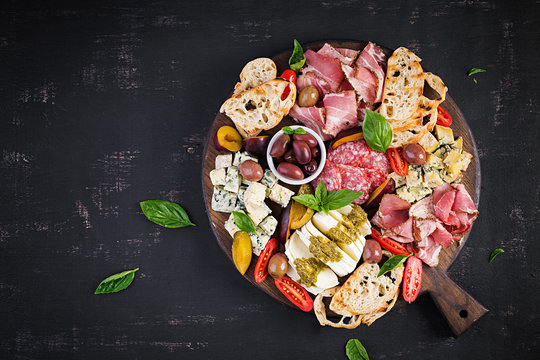 Antipasto platter with ham, prosciutto, salami, blue cheese, mozzarella with pesto and olives on a wooden background. Top view, overhead