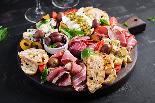 Antipasto platter with ham, prosciutto, salami, blue cheese, mozzarella with pesto and olives on a wooden background.