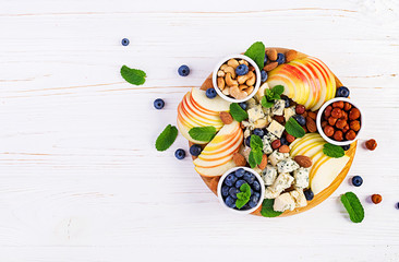 Cheese platter with assorted cheeses, blueberry, apples, nuts on white table. Italian cheese  platter and fruit. Top view, overhead