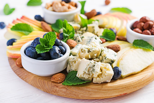 Cheese platter with assorted cheeses, blueberry, apples, nuts on white table. Italian cheese  platter and fruit.