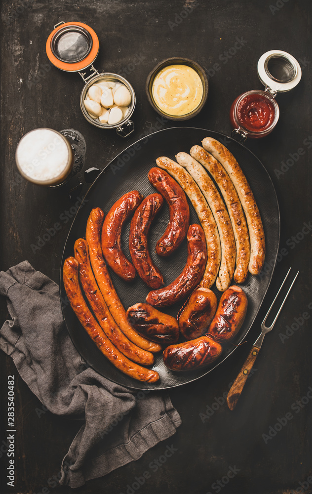 Wall mural Flat-lay of Octoberfest party dinner table concept with grilled veal and pork sausages, sauce, pickled vaggies and beer in glass over dark background, top view