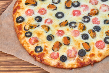 Delicious homemade pizza with seafood on parchment and wooden board. Cooking homemade pizza with shrimp, mussels, black olives and mozzarella. Closeup, selective focus