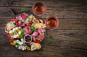 Antipasto platter with ham, prosciutto, salami, blue cheese, mozzarella with pesto and olives on a wooden background. Top view, overhead