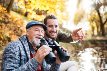Senior father and his son with binoculars and in nature, talking.